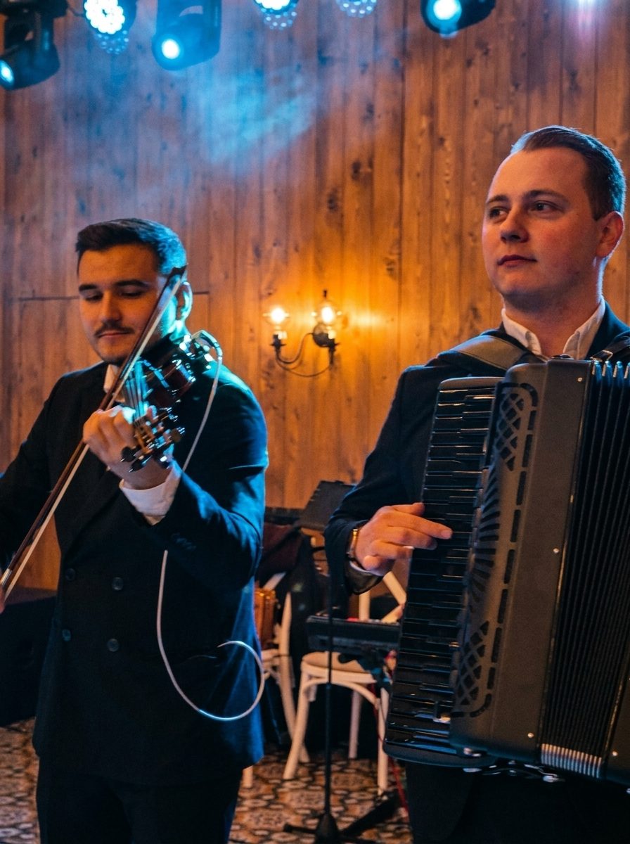 Violonistul și acordeonistul formației cântând la o petrecere